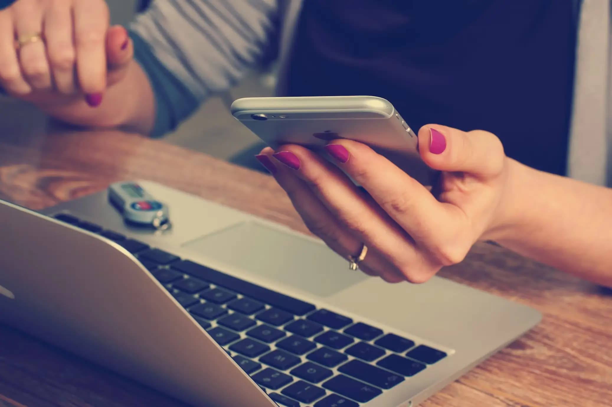 A woman holding an iPhone while sat at her laptop