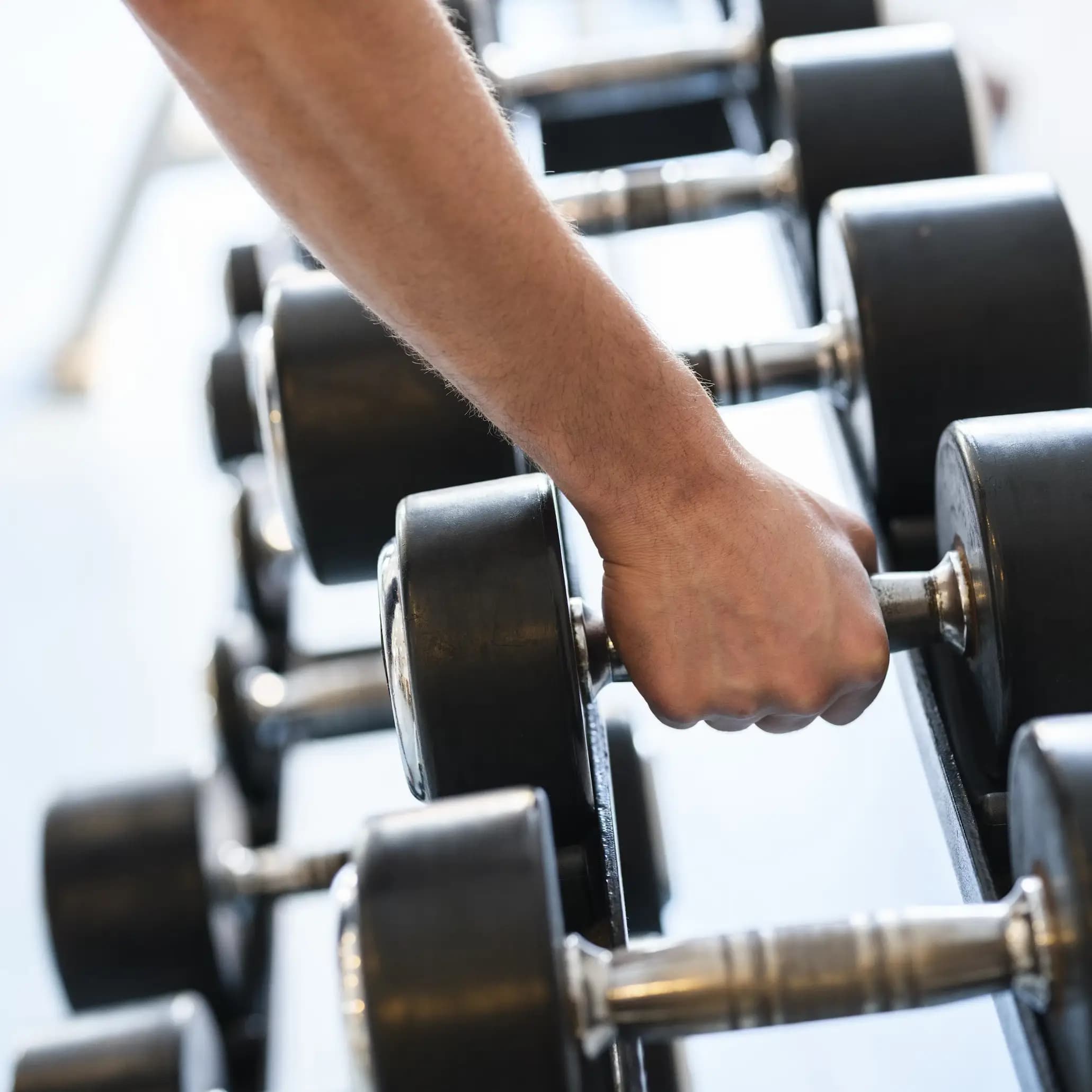 A close up of a hand grabbing a dumbbell from a rack of dummbells