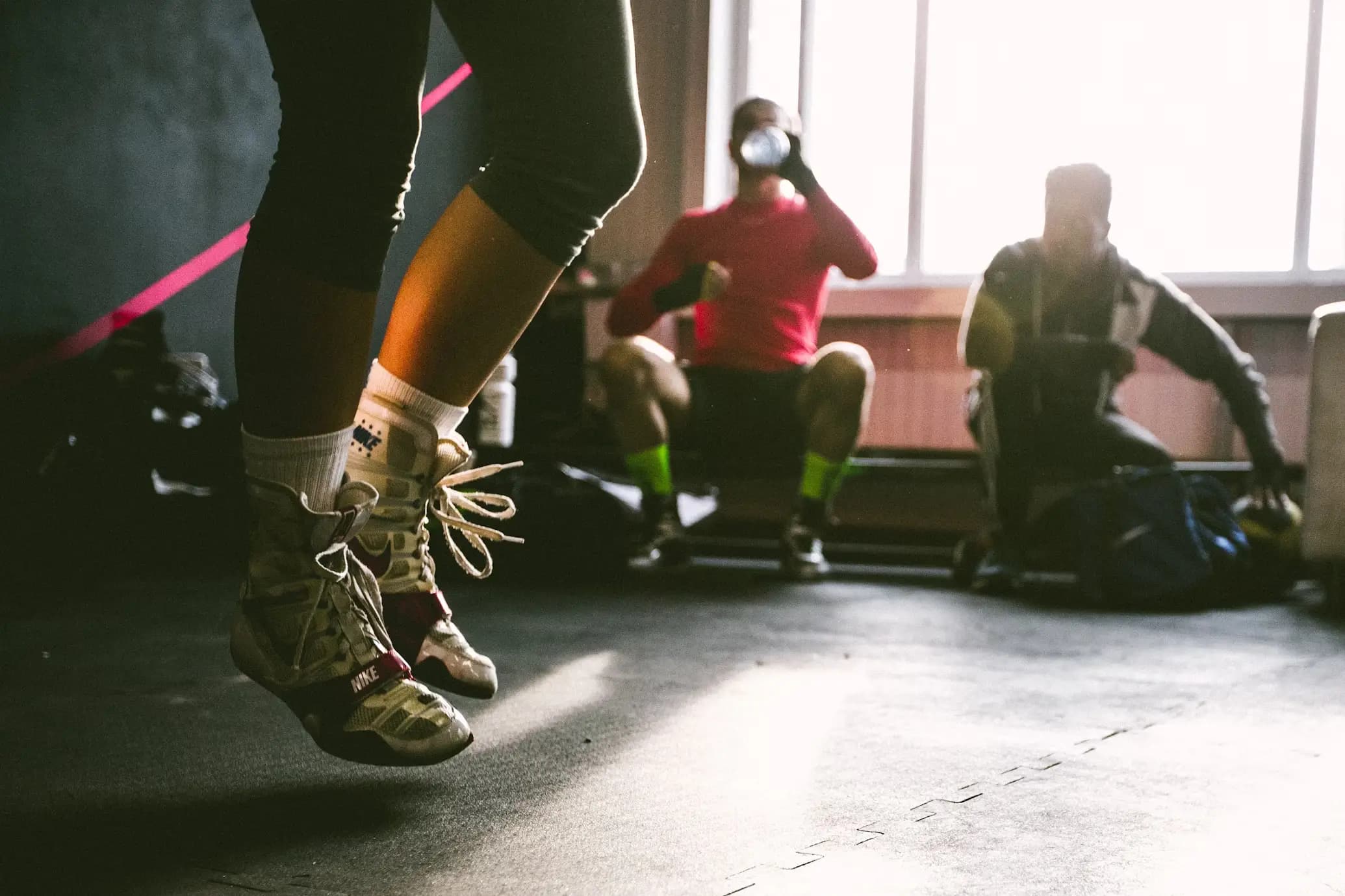 Someone jumping rope in the foreground with two people sitting in the background, one of whom is drinking water