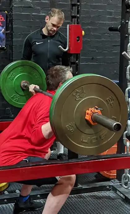 A client performing a squat while being monitored to ensure they are doing it correctly