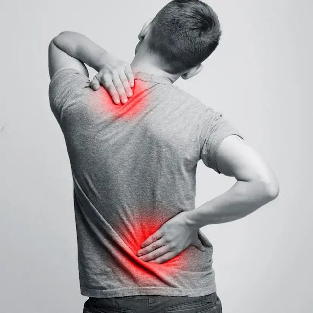 Black and white image of a man taken from behind. He's holding his lower back with one hand and his lower neck with another and there are red marks in these areas indicating pain